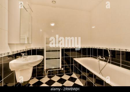 Modernes Bad mit schwarz-weißen Boden- und Wandfliesen sowie stilvoller Badewanne und Waschbecken Stockfoto