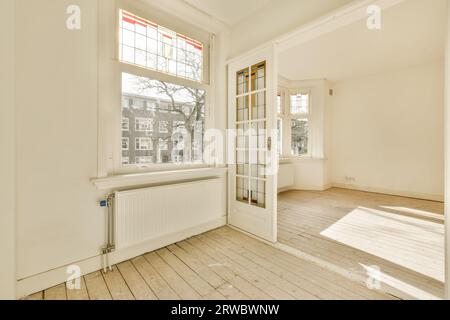 Das Innere des geräumigen, leeren Wohnzimmers mit Sonnenlicht fällt durch große Fenster auf Hartholzboden mit weißen Wänden Stockfoto