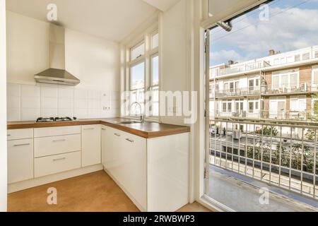 Holztheke mit weißem Schrank und Waschbecken neben großen offenen Fenstern in der modernen Küche des renovierten Apartments Stockfoto