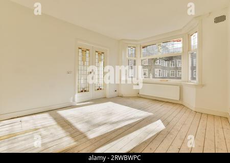 Sonnenlicht fällt durch große offene Fenster auf Hartholzboden in leerem Zimmer mit weißen Wänden in geräumigem Haus Stockfoto