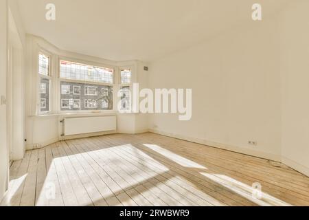 Sonnenlicht fällt durch große offene Fenster auf Hartholzboden in leerem, geräumigem Wohnzimmer mit weißen Wänden Stockfoto