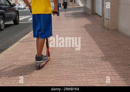 Ein Kind in lässiger Kleidung fährt mit dem Roller auf der Straße, mit dem Rücken zur Kamera. Stockfoto
