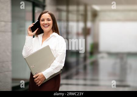 Fröhliche Unternehmerin, Die Über Das Handy Im Modernen Büroinneren Anruft Stockfoto