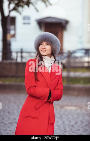 Mädchen in rotem Mantel mit Pelzmütze, die im Schnee posiert Stockfoto