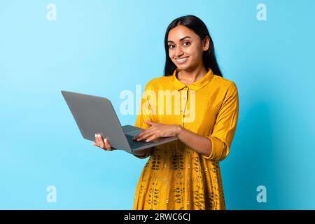 Indische Frau Mit Laptop Posiert In Traditionellem Kleid, Blauer Hintergrund Stockfoto