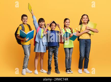 Fröhliche Kinder aus verschiedenen Rassen mit Rucksack und Büchern auf Gelb Stockfoto