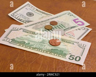 Verschiedene Münzen liegen auf Dollarnoten auf einer braunen Lederoberfläche. Münzen und zwei 50- und eine 5-Dollar-Scheine liegen auf einem braunen Stuhl. Stockfoto