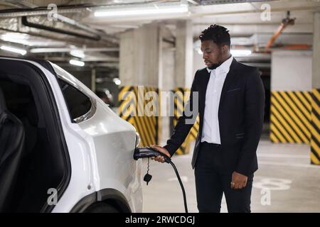 Unternehmer, der das Ladekabel am Parkplatz in das Elektrofahrzeug einsteckt Stockfoto