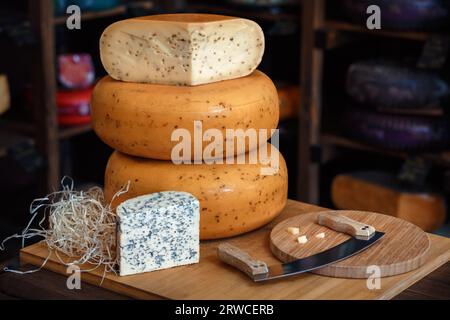 Käseköpfe mit Scheiben und Messern liegen auf einem Holzbrett mit Innenausstattung Stockfoto