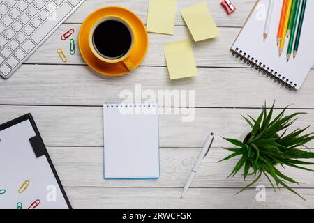 Schreibtisch weiß gelb Tasse Kaffee Notizblock Stifte Aufkleber Gummi Tastatur Maus Ordner Blumenclips Frühling Blumen Tablette Stockfoto