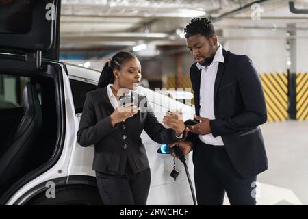 Kollegen, die beim Auffüllen des Elektroautos einen Screenshot ansehen Stockfoto