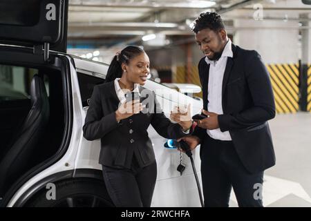 Kollegen, die beim Auffüllen des Elektroautos einen Screenshot ansehen Stockfoto