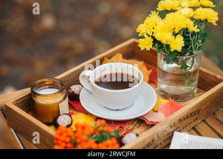 Eine Tasse Tee oder Kaffee auf einem Holztablett vor dem Hintergrund von gefallenen Blättern, Kerze, Herbstsaison, Stillleben mit Blättern, Blumen und Kastanien Stockfoto
