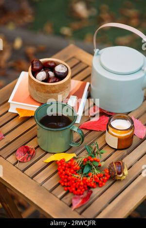Eine Tasse Tee oder Kaffee und ein Buch auf einem Holztisch vor dem Hintergrund von gefallenen Blättern, Herbstsaison, Stillleben mit Blättern, ein Buch und Viburnu Stockfoto