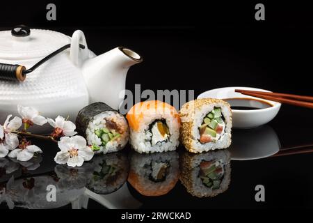 Sushi- und Maki-Brötchen mit weißer Teekanne auf dem Glastisch mit Reflexion Stockfoto