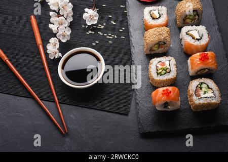 Sushi- und Maki-Brötchen mit weißen Blumenzweigen auf Steintisch. Draufsicht. Stockfoto