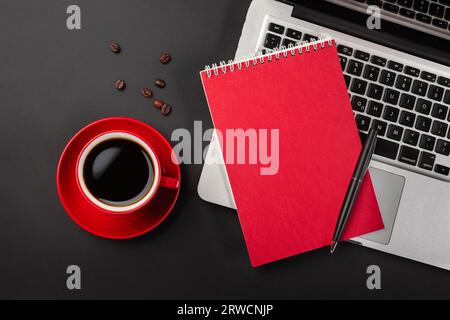 Leerer Notizblock über Laptop und Kaffeetasse auf schwarzem Bürotisch. Draufsicht mit Kopierbereich. Stockfoto