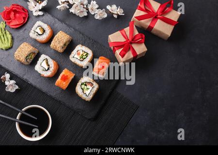 Sushi-Set, Maki-Rollen, Geschenkboxen mit weißem Blumenzweig auf Steintisch, Draufsicht. Stockfoto