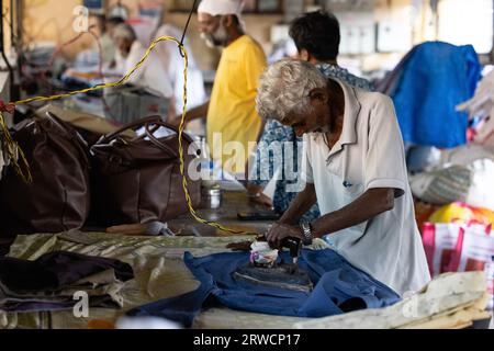KOCHI, INDIEN - 28. JANUAR 2023: Ein Mann bügelt im örtlichen Waschsalon die Wäsche manuell. Stockfoto