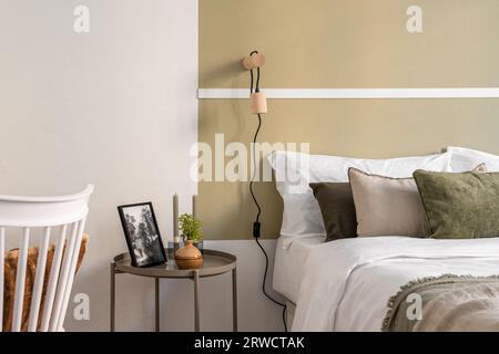 Fragment eines Hotelzimmers in olivbeige Tönen mit einem Doppelbett, einem Nachttisch und dekorativen Accessoires. Das Konzept eines gemütlichen Hotelzimmers für lange Zeit Stockfoto