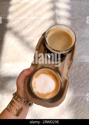 Nehmen Sie schwarzen und weißen Kaffee auf dem Tablett mit einer Frau mit großen goldenen Armbändern Stockfoto