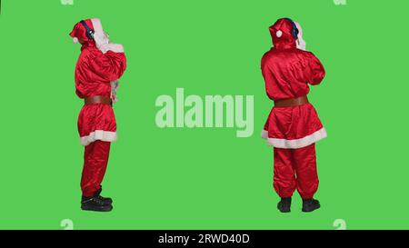 Die Winterfigur tanzt auf Musik, hört moderne Lieder auf dem Headset und trägt ein rotes Kostüm mit Hut. Junger Erwachsener, der die Weihnachtsfeier im dezember mit Kopfhörern genießt. Stockfoto