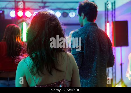 Leute, die auf der Tanzfläche stehen, während sie ein Konzert im Nachtclub mit Scheinwerfern besuchen. In der Diskothek feiern, feiern und tanzen viele Menschen, während Sie die Musik im Rückblick des Clubs genießen Stockfoto