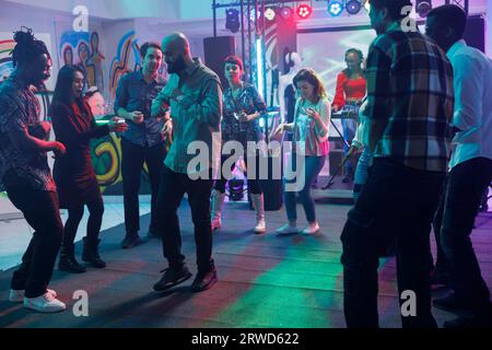 Junge Clubber tanzen in der Diskothek im Nachtclub und feiern zusammen. Verschiedene Leute bewegen sich auf der Tanzfläche während der Party mit Live-Musik-Show im Club am Abend Stockfoto