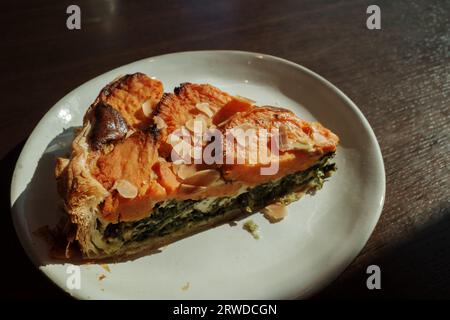 Blick von oben, stimmungsvoller Ton, ein Stück Süßkartoffel- und Spinatkuchen, ein Teller und ein Holztisch unter Sonnenlicht. Stockfoto