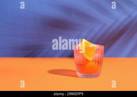 Glas kalter Negroni-Cocktail und Palmenblattschatten auf farbigem Hintergrund Stockfoto
