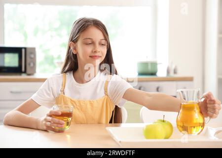 Kleines Mädchen mit Glas und Kanne Apfelsaft in der Küche Stockfoto