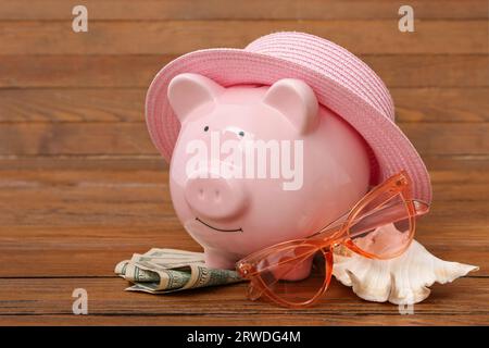 Schweinebank mit Geld und Strandaccessoires auf braunem Holzhintergrund. Konzept der Reisekostenersparnis Stockfoto