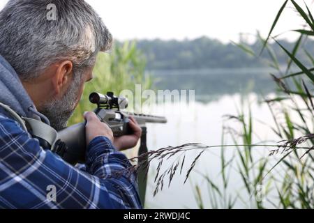 Mann mit Jagdgewehr in der Nähe des Sees im Freien. Leerzeichen für Text Stockfoto