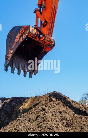 Bagger gräbt Löcher in den Boden. Blick auf die Schaufel des Baggers gegen den blauen Himmel auf einem Erdhaufen. Baustelle. Hintergrund. Stockfoto