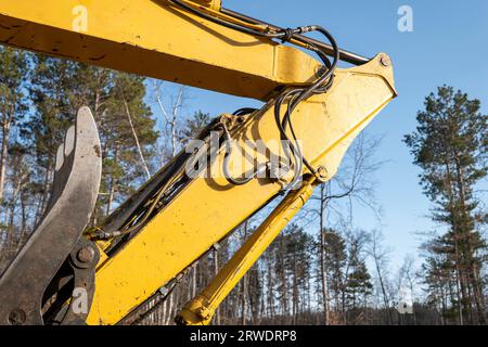 Das Kniestück des Auslegerarms und die Hydraulikschläuche an einem schweren Bagger auf einer neuen Baustelle mit blauem Himmel und Bäumen im Hintergrund Stockfoto