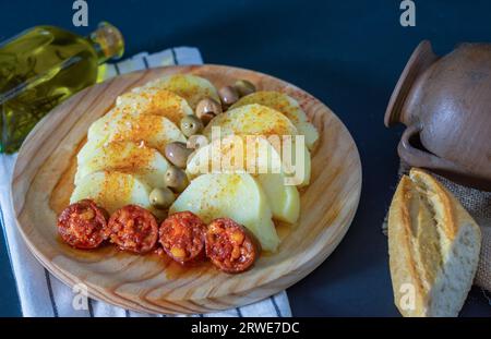 Gekochte Kartoffel mit Paprika und gebratenem Chorizo auf einem Holzbrett mit einer Flasche nativem Olivenöl extra mit Rosmarin Stockfoto