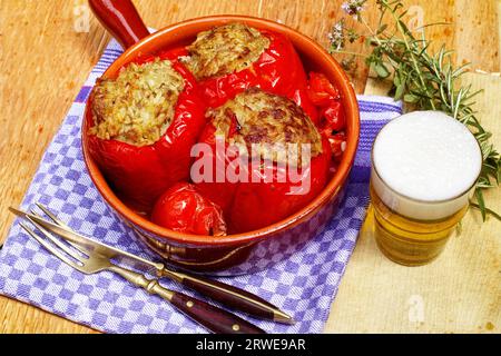 Rote Paprika, gefüllt mit Hackfleisch in einer Auflaufform. Rechts ein Glas Bier. Vordergrundgabel und -Messer Stockfoto