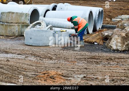 Ein Bauarbeiter in einem Helm und einem Bademantel arbeitet mit einer industriellen Eisensäge auf einer Baustelle mit einer Industriesäge. Stockfoto