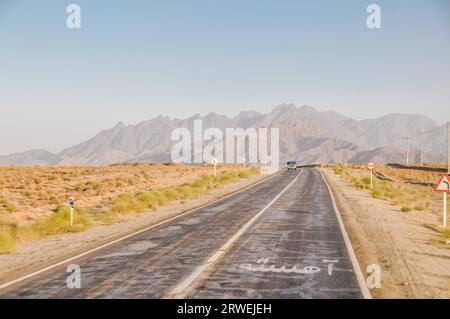 Foto einer leeren Straße mit einem Auto in der Entfernung, umgeben von Bergketten in Kaschan im Iran Stockfoto