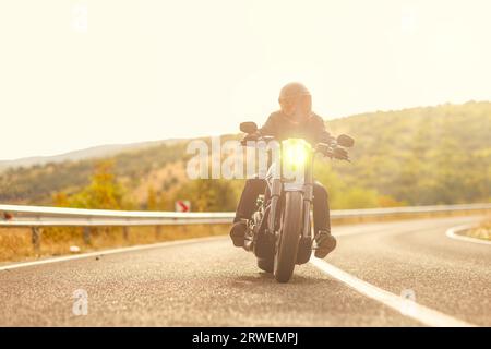 Mann mit Helm, der bei Sonnenuntergang auf einem Chopper-Motorrad auf einer offenen Straße reitet Stockfoto