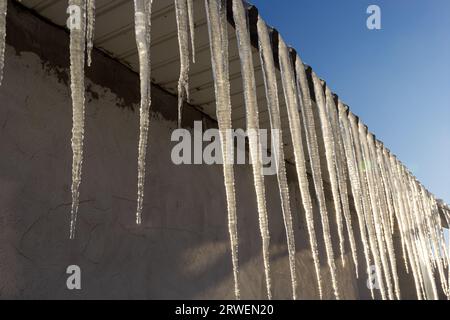 Scharfe Eiszapfen und geschmolzener Schnee hängen von den Dachtrassen. Wunderschöne, transparente Eiszapfen, die langsam über ein Dach gleiten. Stockfoto