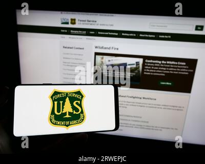 Person, die ein Mobiltelefon mit dem Logo des United States Forest Service (USFS) auf dem Bildschirm vor der Webseite hält. Konzentrieren Sie sich auf das Display des Telefons. Stockfoto