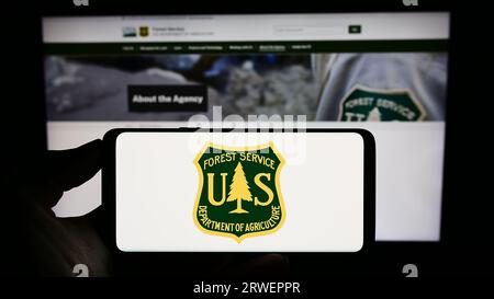 Person, die ein Mobiltelefon mit dem Logo des United States Forest Service (USFS) auf dem Bildschirm vor der Webseite hält. Konzentrieren Sie sich auf das Display des Telefons. Stockfoto