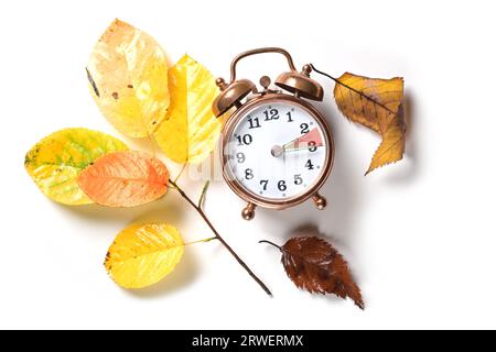 Fallen Sie im Herbst nach der Sommerzeit auf einen Vintage-Wecker zurück und einige farbige Blätter auf weißem Hintergrund, flache Lage, Kopierraum, Stockfoto