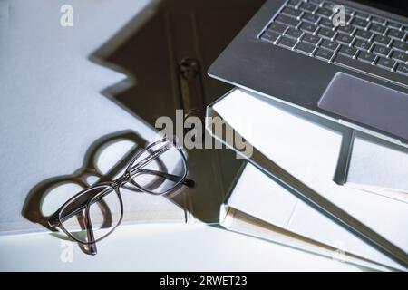 Brillen und ein Teil eines Laptops auf weißen Aktenordnern mit scharfen Schatten auf einem Büroschreibtisch, Geschäftskonzept, Kopierraum, ausgewählter Fokus, schmal d Stockfoto