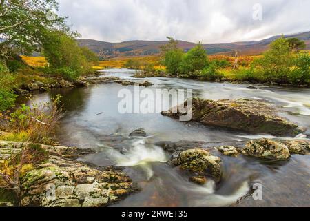 Der Fluss Farrar fließt schnell über moosbedeckte Felsen in Glen Strathfarrar, Highlands of Scotland. Eine herbstliche Szene mit goldenen Bracken, Bergen Stockfoto