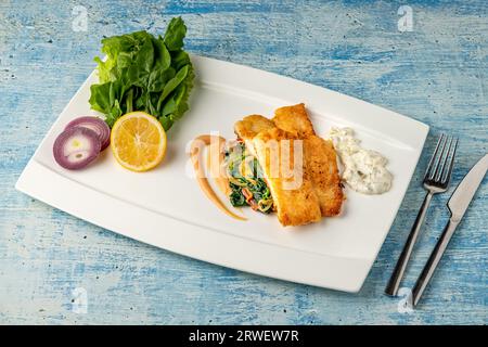 Gebratenes Panga-Filet mit Gemüse und Zwiebeln an der Seite und Spinat darunter Stockfoto