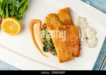 Gebratenes Panga-Filet mit Gemüse und Zwiebeln an der Seite und Spinat darunter Stockfoto