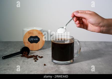 Die Hand der Frau hat Steviasüße in einen schwarzen Kaffee gesteckt, grauer Hintergrund Stockfoto