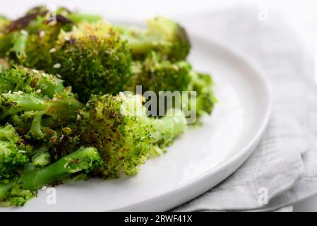 Brokkoli-Blütenstände, gebraten mit Gewürzen und Sesamsamen auf einem Teller auf einem weißen Tisch. Nahaufnahme. Stockfoto